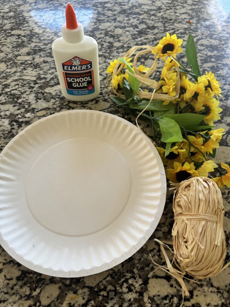 art supplies on the counter elmers glue fake flowers paper plates and string