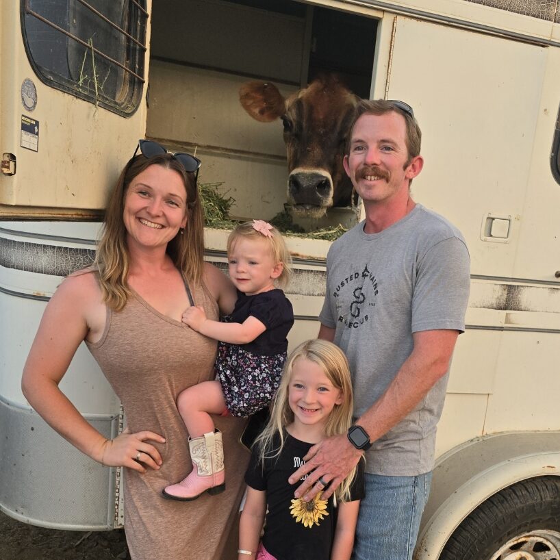 family standing in front of a trailer with a jersey cow poking her head out